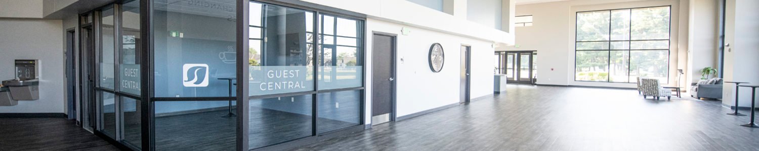 Wide view of the church lobby featuring a glass-enclosed 'Guest Central' area, high ceilings, and polished flooring.