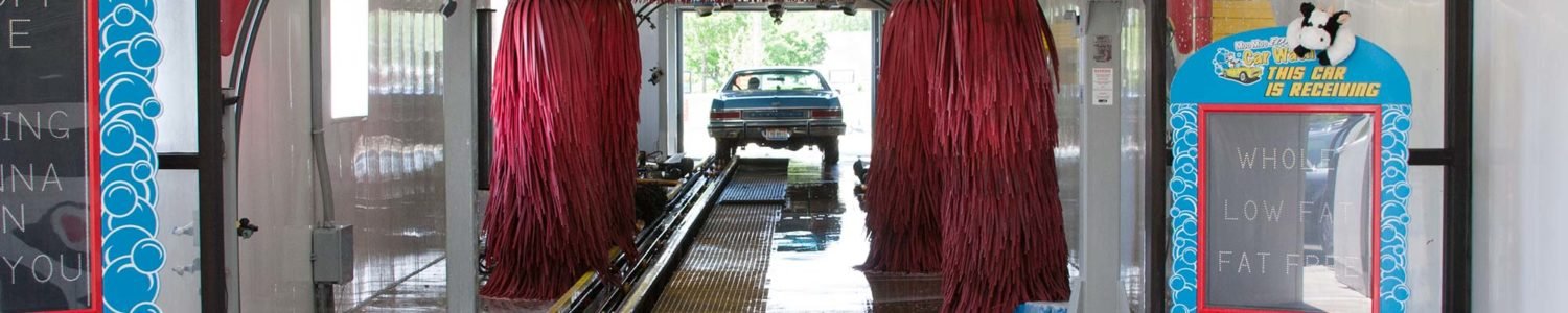 Interior of the car wash tunnel with large red rotating brushes and water spraying, defining the automatic washing equipment.