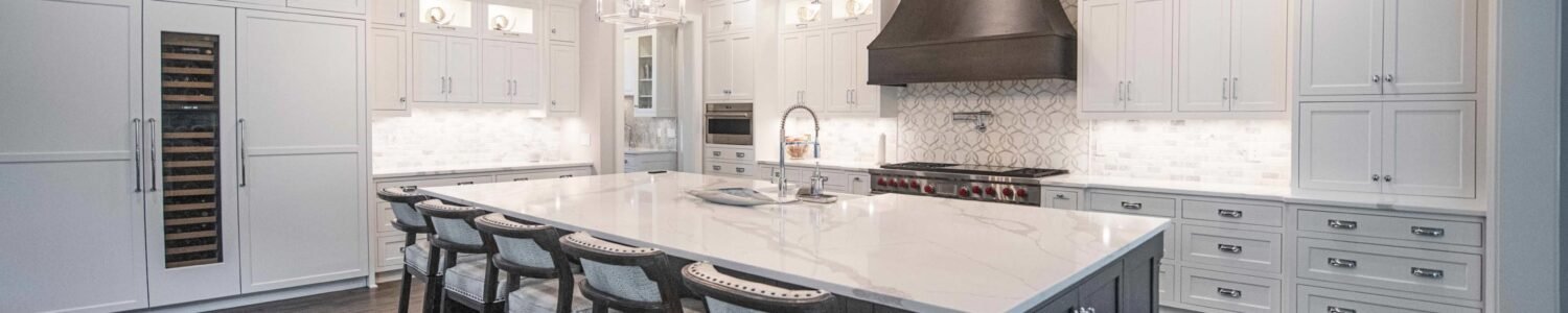 Spacious contemporary kitchen with white perimeter cabinets, a large dark central island with seating, a white countertop, and an imposing dark metal range hood.