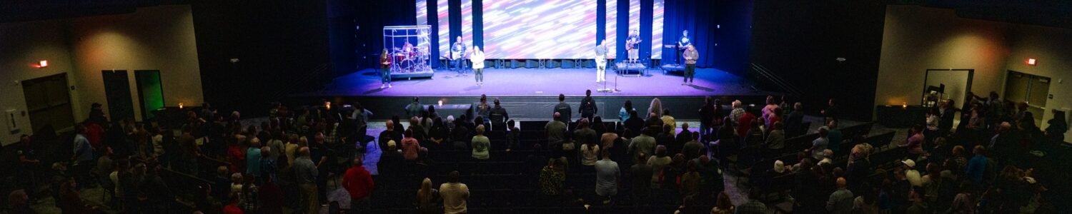 Large church worship space or auditorium featuring an expansive stage with extensive lighting, and multiple large LED screens.