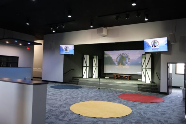 Wide view of the church's renovated worship space, showcasing the stage with a large screen, side display monitors, and decorative light columns.