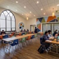 Interior rendering of the Franklinton High School commons with students at tables and a colorful geometric mural