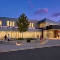 Rendering of the Granville Christian Academy entrance at dusk with lit glass storefront, tree-lined plaza and curved concrete seating